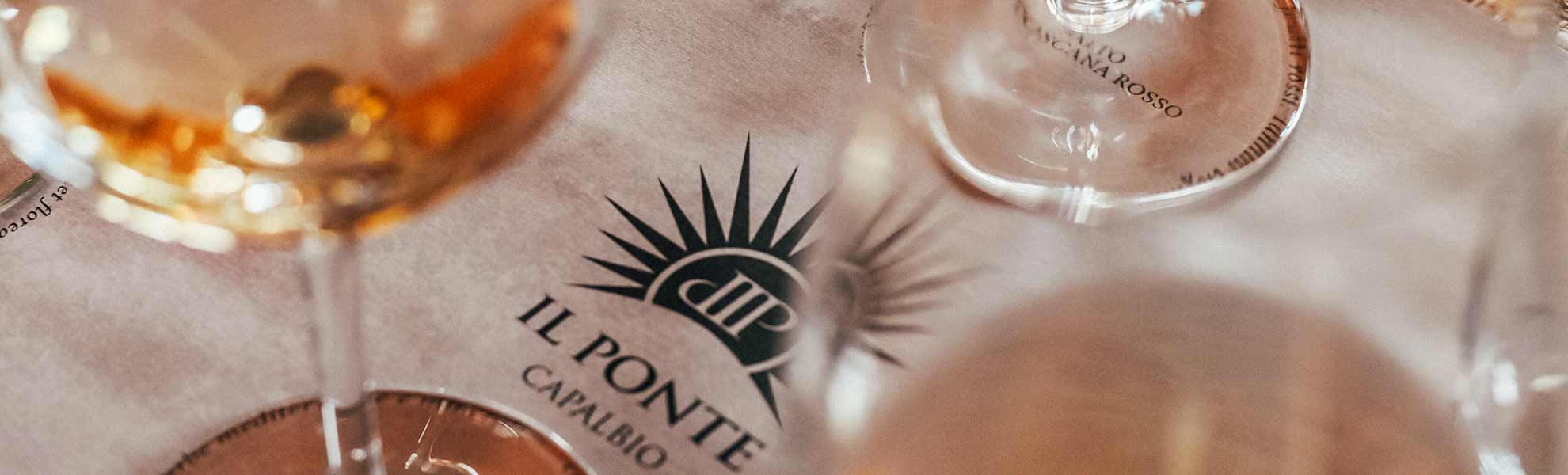 Il dettaglio di una tavola con una tovaglietta con il marchio di Agricola Il Ponte - Capalbio